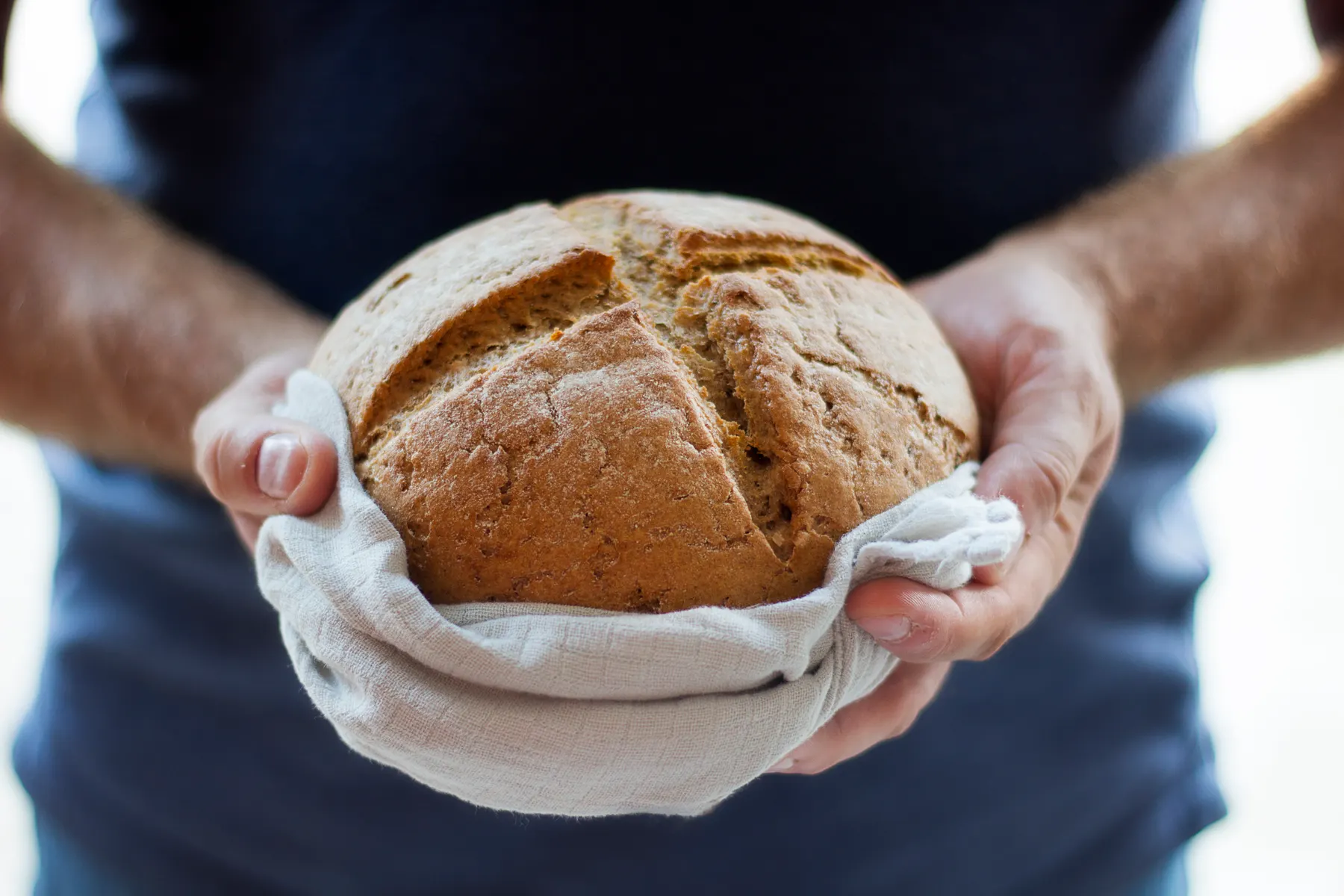 Baker holding a freshly baked round sourdough loaf wrapped in a linen cloth