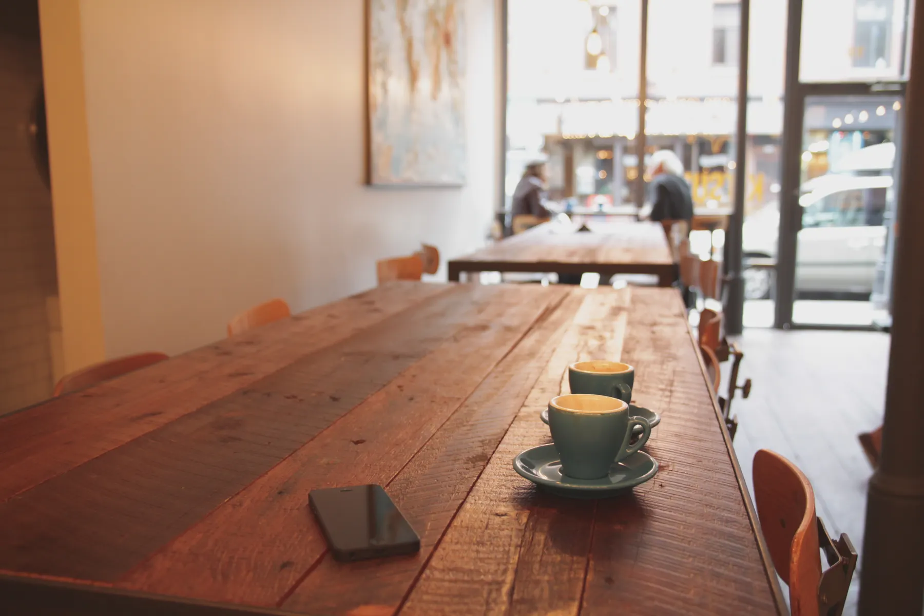 Long wooden communal table with a single coffee cup on it